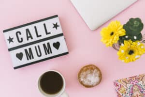 Lightbox avec inscription « Call Mum » entourée de fleurs jaunes, d'une tasse de café et d'un donut sur fond rose